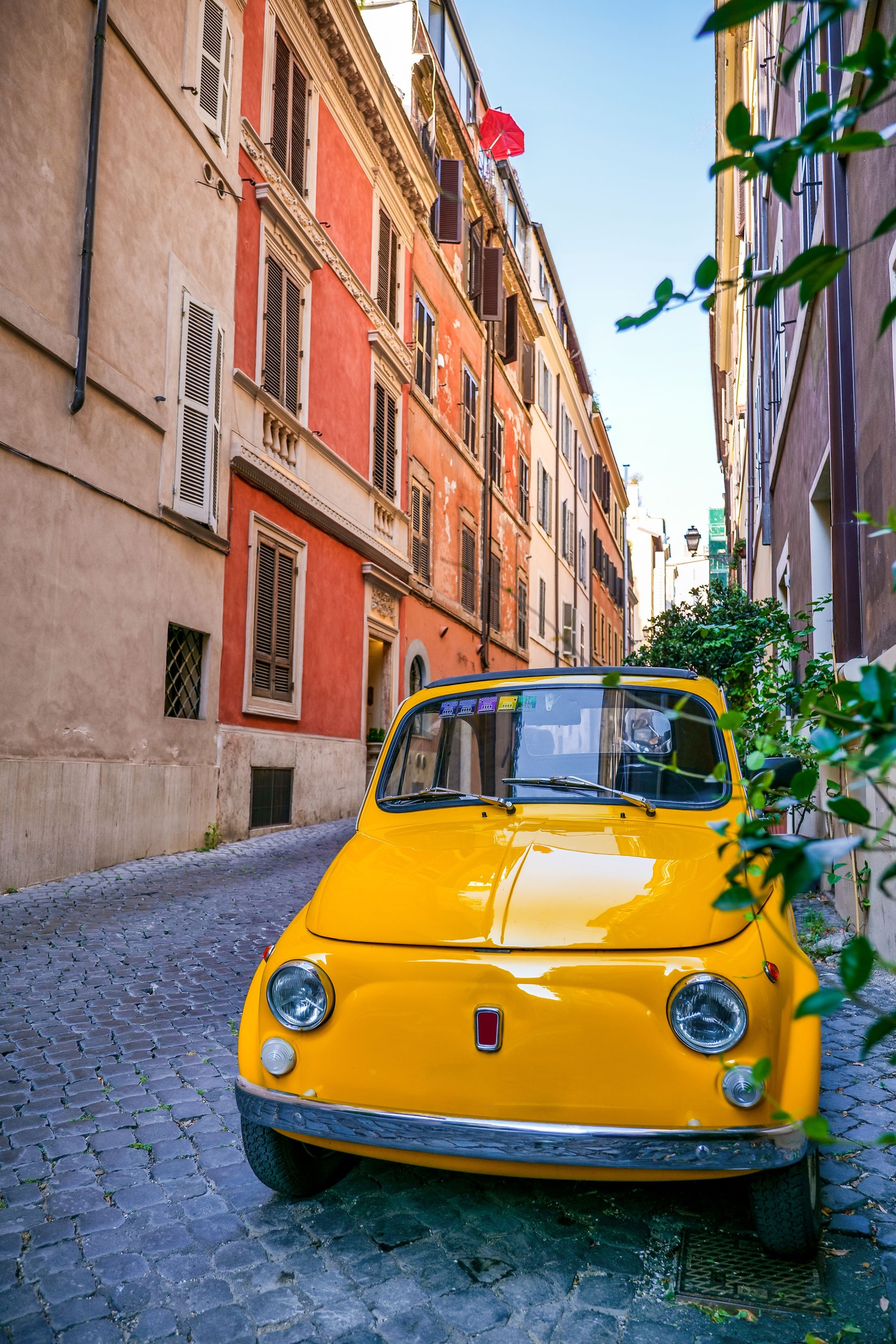 A vintage yellow Fiat 500 parked along a stone alley in the Monti district in the historic heart of Rome